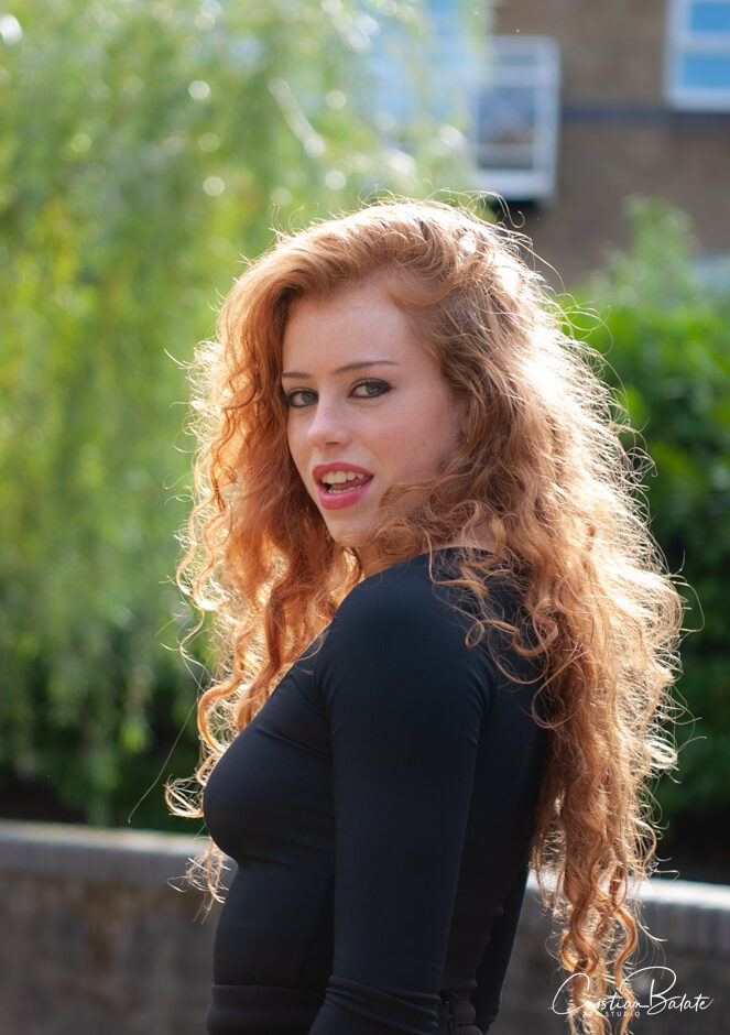 Side view of freckled blonde woman smiling at camera from half profile while participating in summer photo shoot on a sunny day