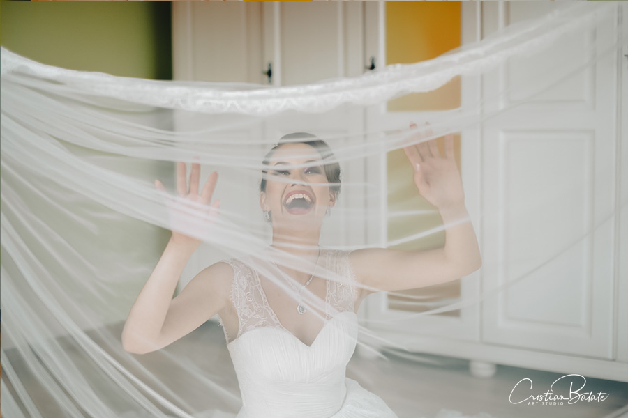 The bride playing behind the white veil on the wedding day inside the house smiling happily